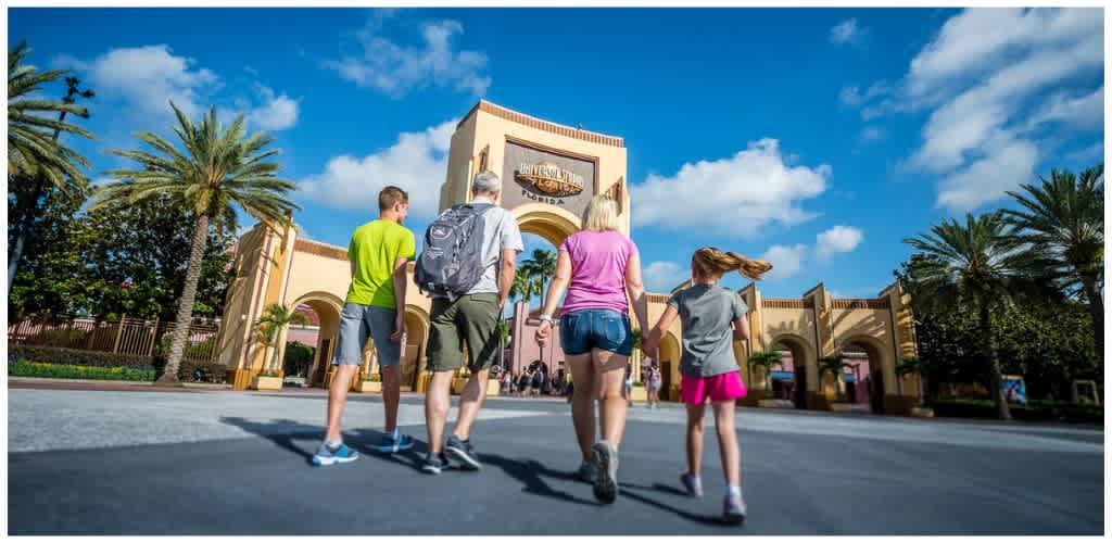 Family walking towards Universal Orlando Resort entrance on sunny day with palm trees and blue sky