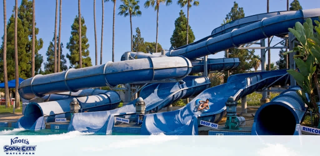 A child slides down a blue water slide at Knott's Soak City water park with multiple twisting slides and palm trees in the background