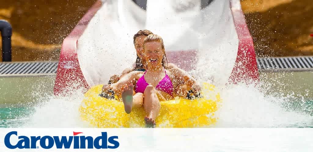 Three people on a yellow raft splash down a water slide.