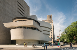 Image of a white, curvilinear building with smooth, horizontal bands against a blue sky with fluffy white clouds. The structure's design creates an elegant, flowing appearance, reminiscent of modern architecture.