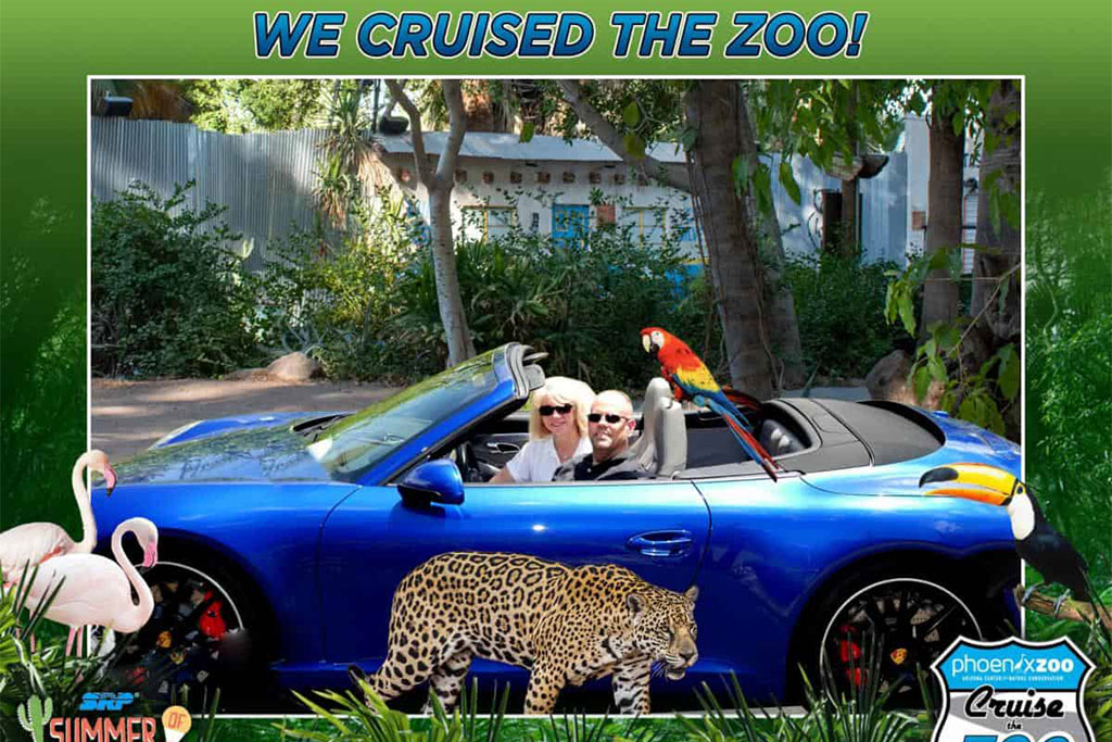 Two people with a parrot in a blue convertible at a zoo-themed photo booth.