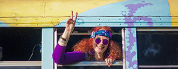 Image Description: In this photo, we see an individual expressing joy with a peace sign gesture, leaning out of a bus window. The bus has a retro design, featuring a vibrant yellow color with what appears to be a blue and purple wave pattern on the side. The person is wearing purple circular sunglasses, a patterned headband, and a purple top, giving off a cheerful, hippie vibe. Their hair is curly and reddish in color, complementing the upbeat and colorful aesthetic of the scene.

FunEx.com is committed to bringing you the best experiences at the lowest prices, so don't miss out on our exclusive discounts on tickets to make your next adventure as memorable as a peace sign out of a vintage bus window.