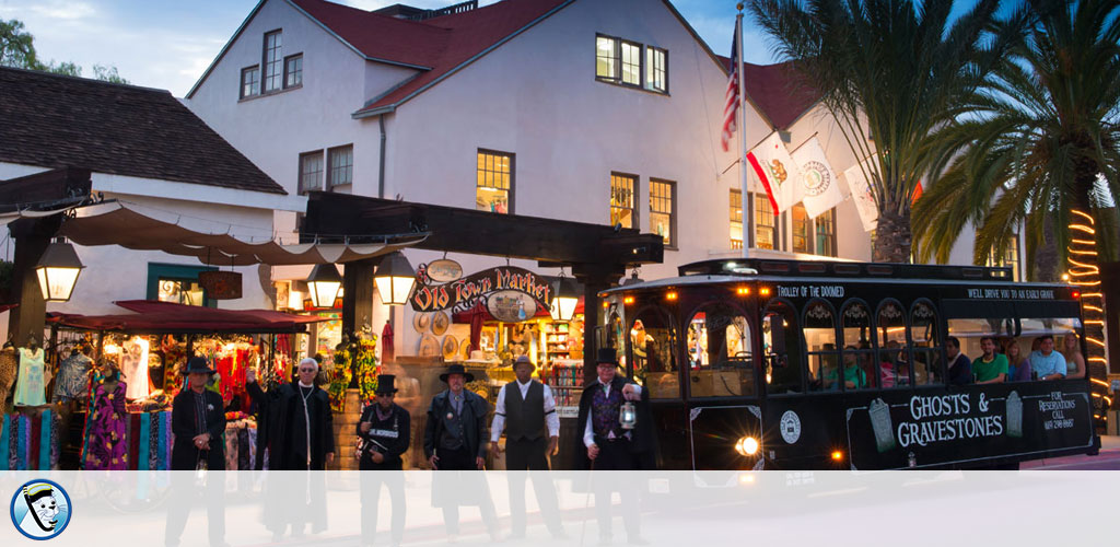 Dusk view of a trolley tour by a market with people, palm trees, and twilight sky.