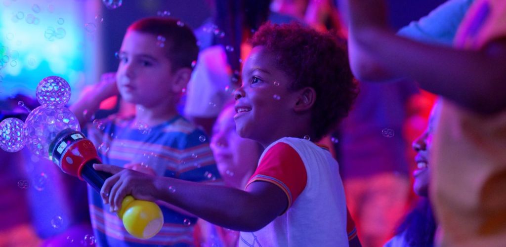 Children playing with a bubble gun in colorful, vibrant lighting at Funex site