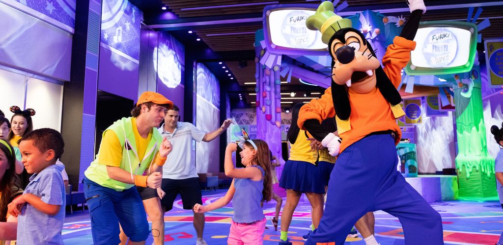 Children and adults dance and have fun with a large Minnie Mouse mascot in a colorful indoor entertainment setting. Bright lights and playful decor enhance the lively atmosphere.