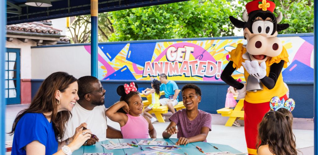Children and adults enjoy a themed party outdoors with a life-sized Minnie Mouse mascot, colorful decorations, and a sign that says get animated.