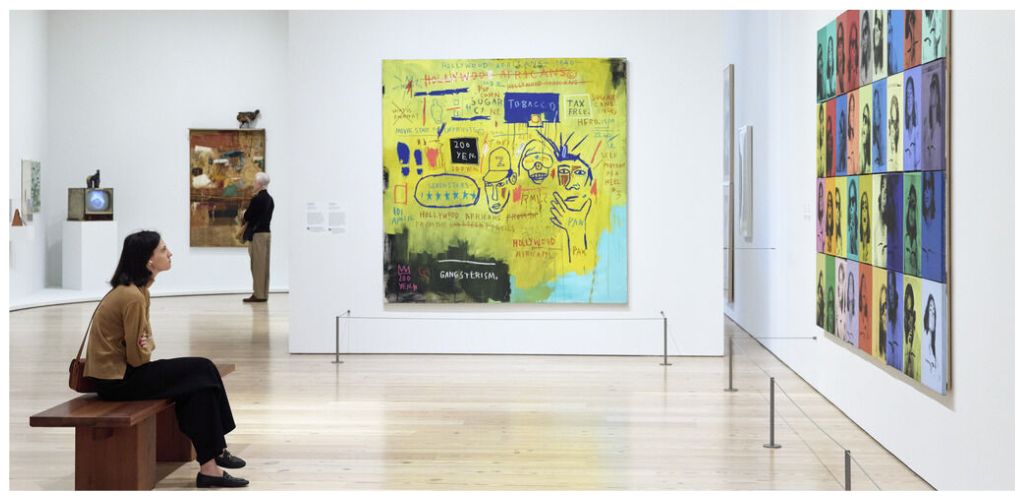Woman sitting on bench observing colorful abstract and pop art paintings in a modern museum gallery
