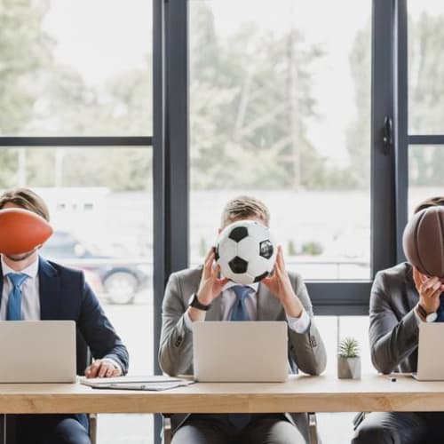 Three office workers holding different sports balls in their hands