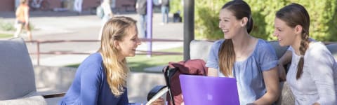 Three girls sit and chat about GCU tuition costs on outdoor bench with an open laptop on lap