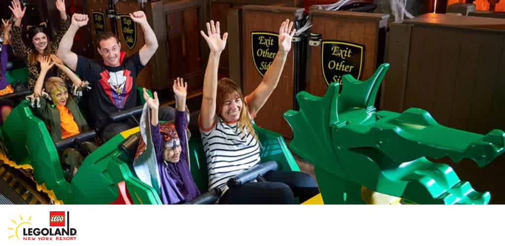 People riding a green dragon-themed roller coaster at Legoland New York Resort with arms raised.