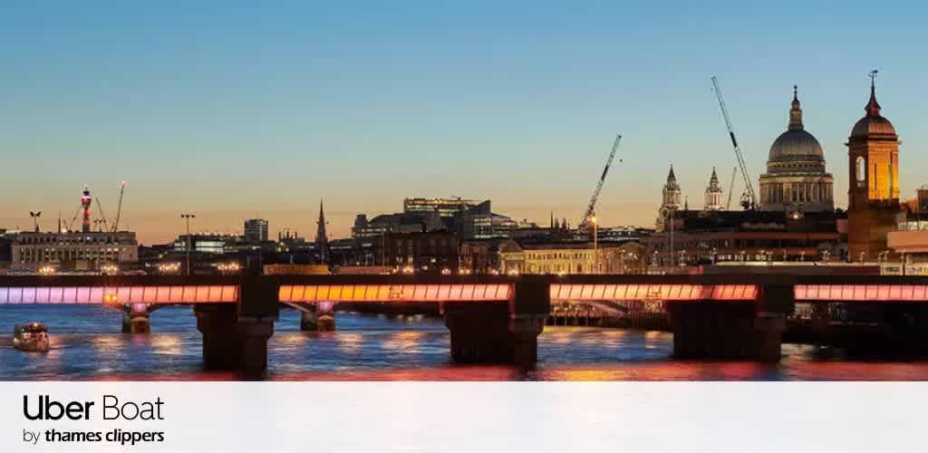 A city skyline at sunset featuring historic and modern buildings, cranes, and a river with a bridge illuminated in pink.