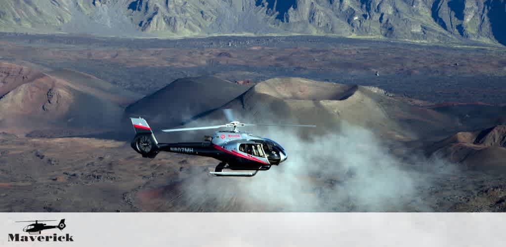 A helicopter with red and black markings, labeled Maverick, flies over a rugged desert landscape with mountains in the background, kicking up a trail of dust beneath. The sky is clear and blue above the earthy tones of the desert terrain.
