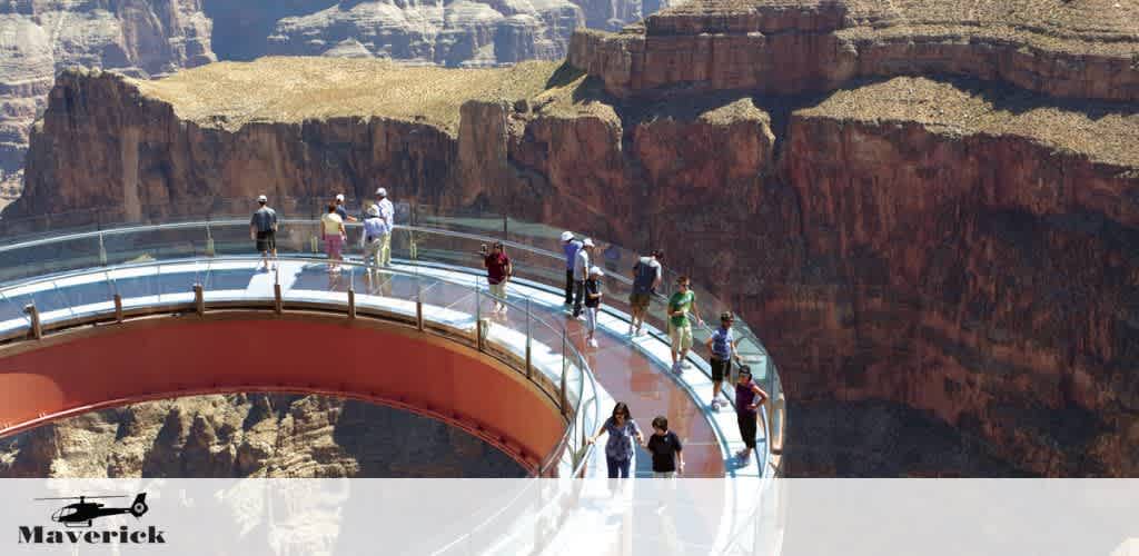 Visitors explore the Grand Canyon Skywalk, a horseshoe-shaped glass walkway extending over the canyon. The clear platform offers a stunning view of the rugged landscape below under a clear blue sky. A Maverick helicopter logo is visible in one corner.