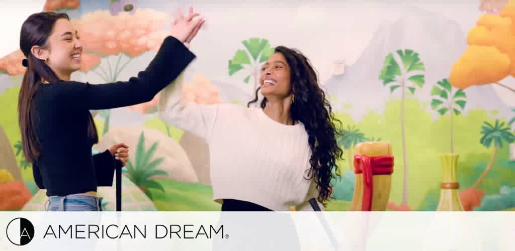 Two women high-fiving in front of a colorful mural with golf props, with the text