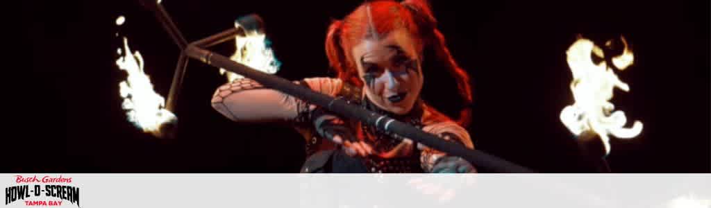 Performer with red hair manipulating a flaming baton against a dark background.