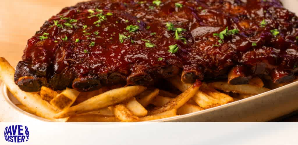 Barbecue ribs with sauce and herbs on a bed of fries, with Dave & Buster's logo.