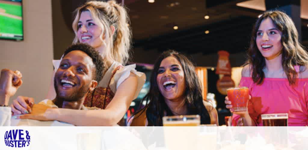 Four people smiling and enjoying drinks in a lively indoor setting.
