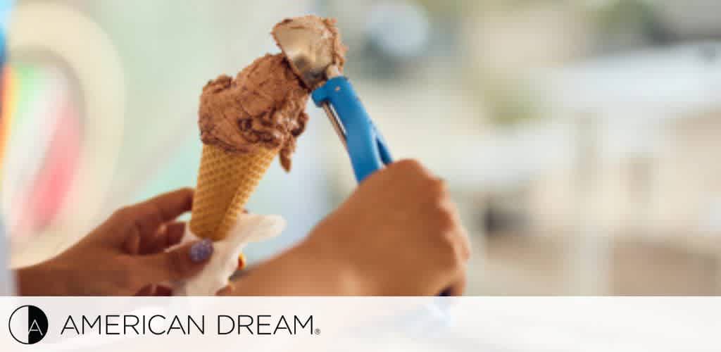 A person scooping chocolate ice cream onto a waffle cone.