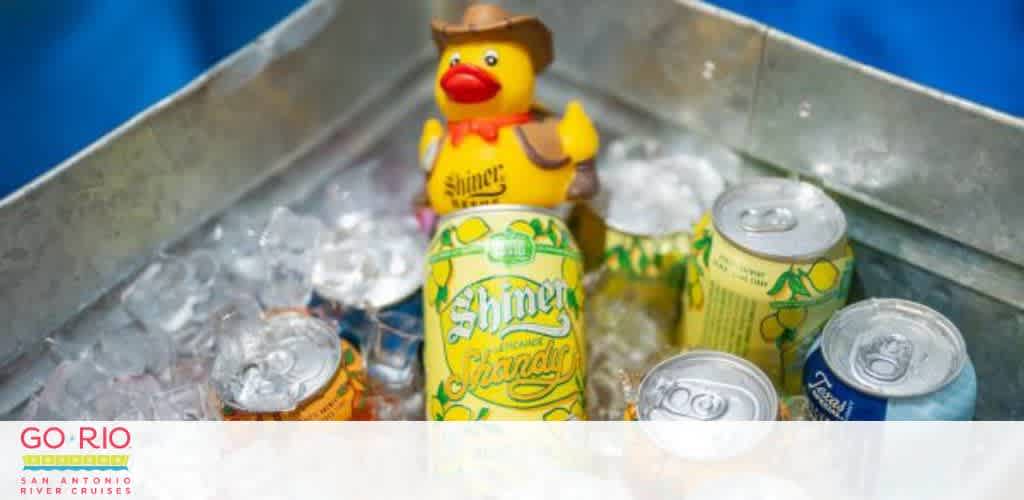 A metal ice chest with canned drinks, ice, and a yellow duck in a cowboy hat marked