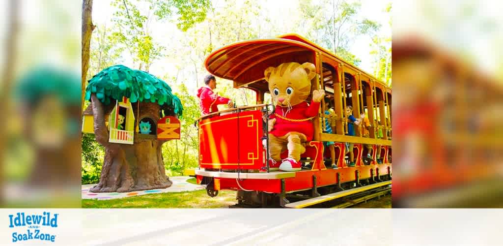 A vibrant scene at Idlewild and SoakZone features a colorful trolley with a friendly character in a red outfit at the front. The trolley is set in a lush, green park with trees and a whimsical treehouse visible in the background. The playful atmosphere suggests an exciting and family-friendly adventure.