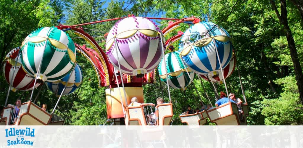 Brightly colored balloon-themed ride at Idlewild and SoakZone set against lush green trees. Children and adults are seated in suspended baskets, enjoying the sunny day and the gentle ride. The vibrant colors and joyful atmosphere make it an appealing attraction for families.