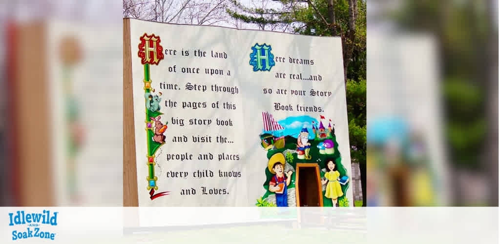 The image shows a large storybook display with colorful illustrations of fairy tale characters and a castle. The text reads: Here is the land of once upon a time. Step through the pages of this big storybook and visit the people and places every child knows and loves. Here dreams are real and so are your storybook friends. The Idlewild and SoakZone logo appears in the corner. Trees can be seen in the background.