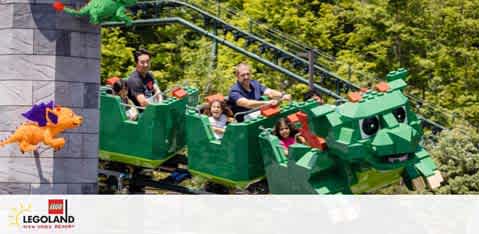 Image shows a group of people enjoying a ride at LEGOLAND. They are seated in a green, dragon-themed roller coaster car. The front car resembles a friendly dragon’s head. A LEGO fire-breathing dragon sculpture is visible to the side, enhancing the playful ambiance of the ride.