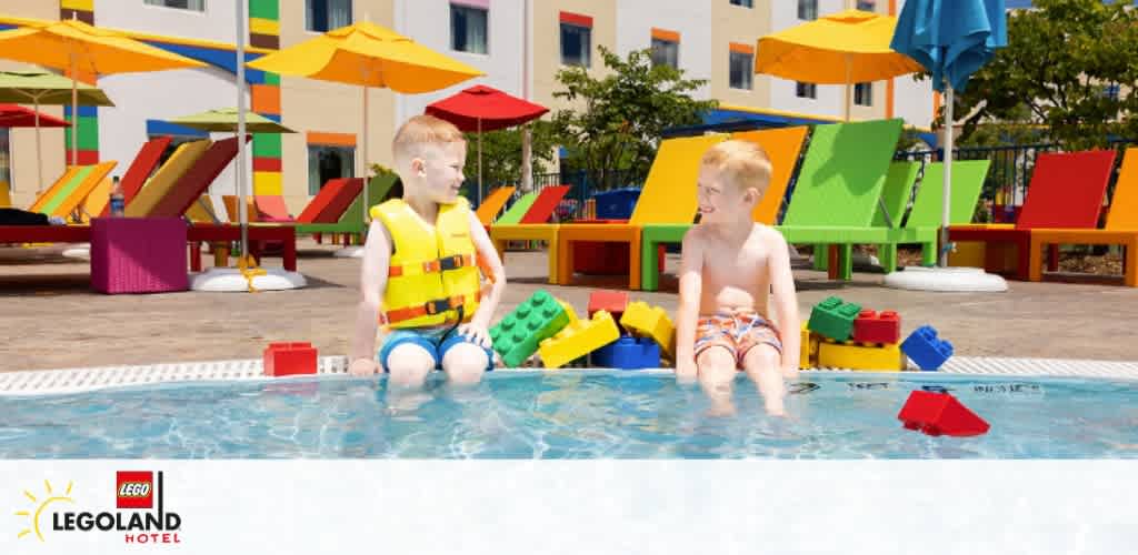 A pirate-themed room at LEGOLAND Hotel with a family enjoying playtime. A child wearing a pirate hat stands on the bed with a sword. Another child holds a shield. Two adults in the background cheer and play along with joyful expressions. The room features bright red and white striped walls and wooden decor.