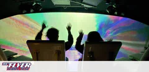 This image displays the silhouette of two individuals experiencing a virtual ride attraction. They are seated, clearly visible from behind, with their hands up in the air, suggesting excitement and involvement in the action. The ride is enclosed, with a large, curved screen in front of the participants. The screen fills their view with vibrant colors that resemble swirling nebulas and cosmic phenomena, implying a space or flight simulation experience. Lighting effects enhance the immersive atmosphere, contributing to the anticipation of an exhilarating adventure that awaits the riders. The text "THE FLYER - San Francisco" appears at the bottom, indicating the name and location of the attraction.
Experience the thrill of THE FLYER - San Francisco and explore an array of amazing adventures at GreatWorkPerks.com, where the excitement is matched only by our commitment to savings with the lowest prices on tickets.
