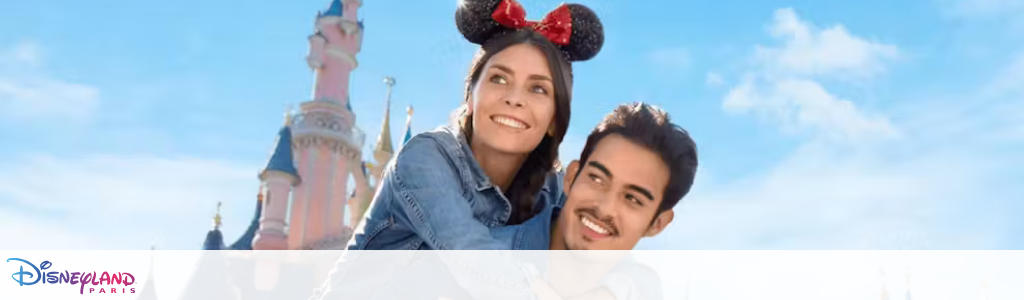 A joyful woman wearing mouse ears is being lovingly carried on a man's back. Both are smiling and looking happy. In the background, the iconic Disneyland Paris castle stands against a bright blue sky, symbolizing fun and adventure.