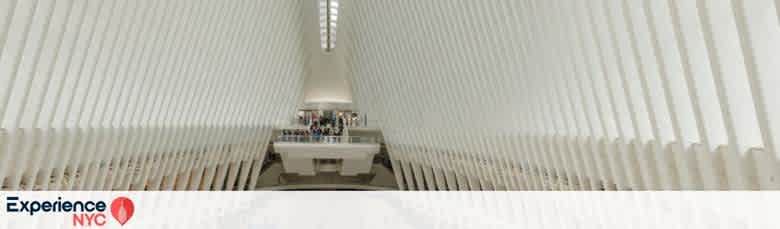 Interior view of the Oculus at the World Trade Center Transportation Hub in NYC. The architectural design features a series of white, rib-like structures that converge at the ceiling, creating a bright and spacious atmosphere. In the background, a mezzanine with people can be seen, emphasizing the space's grandeur and functionality. The bottom of the image shows the text Experience NYC with a red location pin icon.