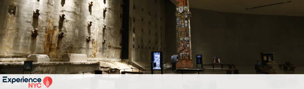 The image shows a spacious museum exhibit with a high wall featuring large, rusty tiebacks. A tall, art-covered column stands prominently in the center, surrounded by displays and information panels. The space is dimly lit, creating a reflective atmosphere. In the foreground, the words Experience NYC are visible.