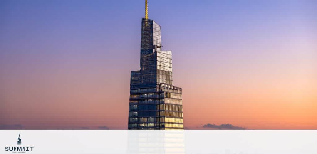 The top of SUMMIT One Vanderbilt gleams at sunset against a colorful sky, showcasing its sleek, angular glass architecture and spire, standing prominently above the horizon.