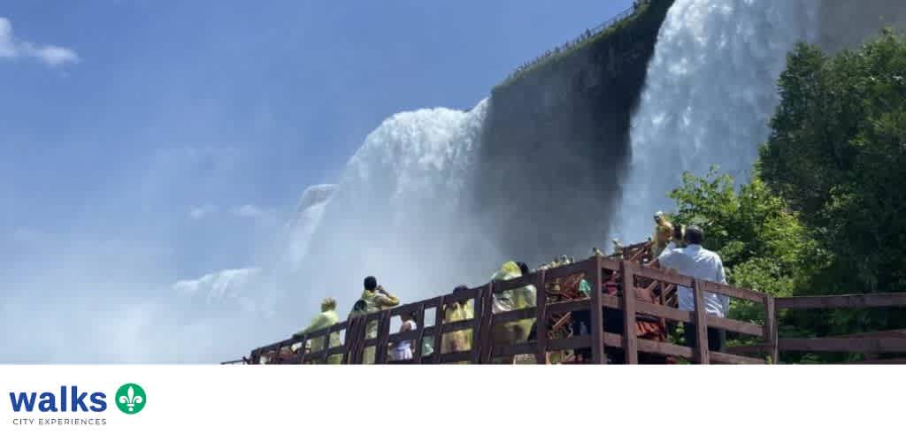 Tourists standing on a viewing platform overlooking a large waterfall with lush green trees in the background