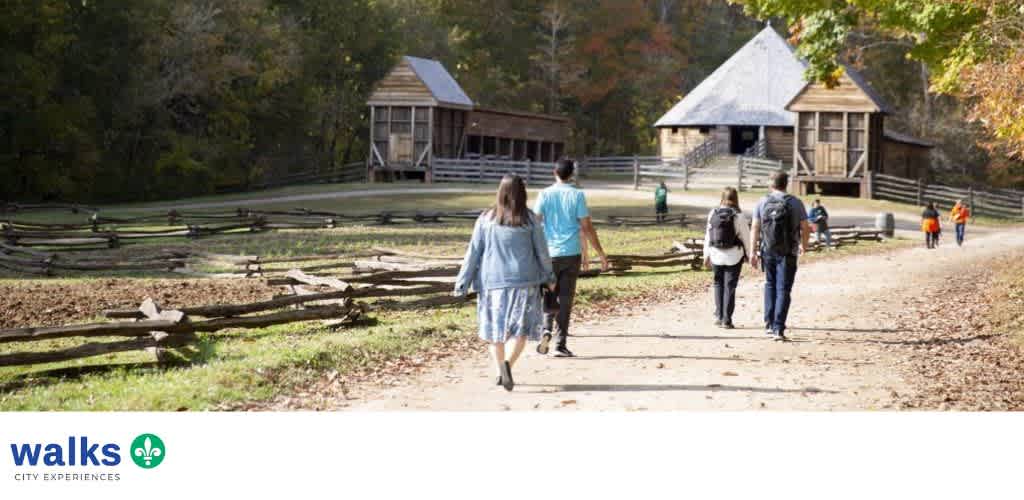 Group of people walking along a path in a park with wooden buildings and autumn trees in the background