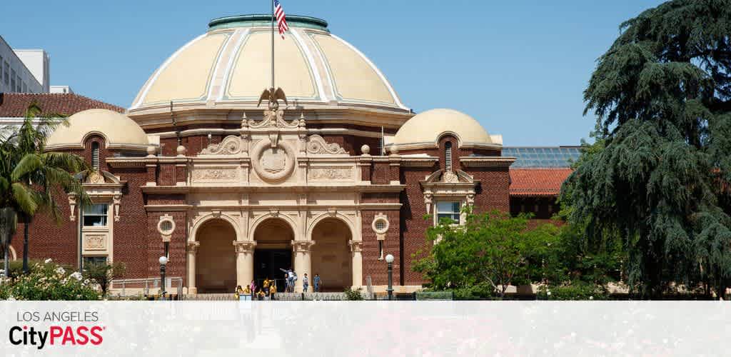 Historic building with a domed roof, brick facade, surrounded by trees, with people entering through arched entrances