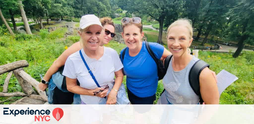 A group of four people are smiling outdoors on a lush, green path in New York City. They appear to be on a walk or hike, enjoying the natural surroundings. The text Experience NYC is visible in the bottom left corner of the image.