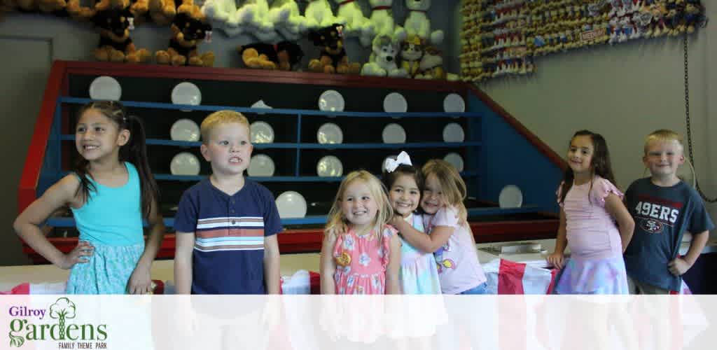 Group of smiling children standing indoors at Gilroy Gardens family theme park with stuffed animals in the background