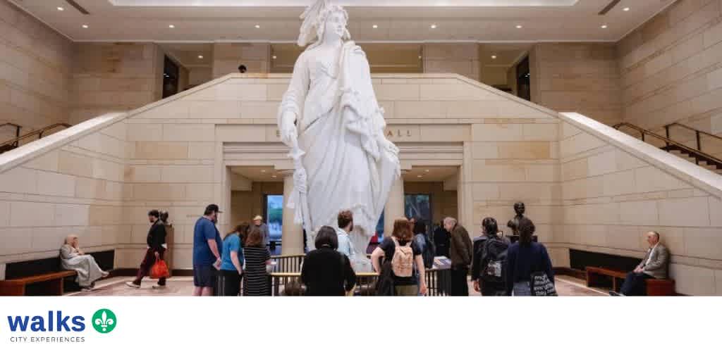 Visitors gather around a large white sculpture in the Grand Hall of a museum with seating on either side.
