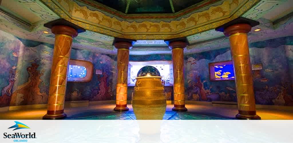 Interior view of a themed room at SeaWorld Orlando with ornate, underwater-style decor. Golden pillars support a painted ceiling, while walls feature aquatic murals and fish tanks. A branded logo appears in the image's lower right corner.