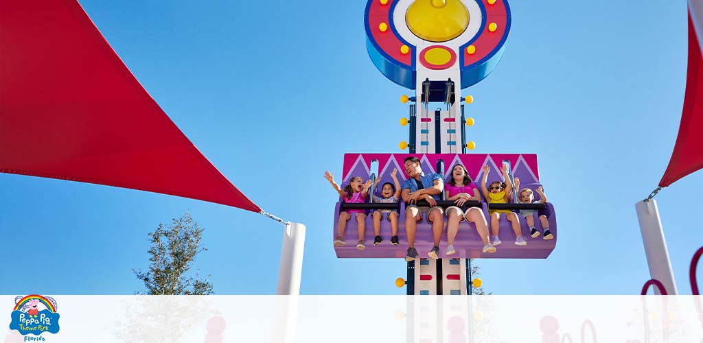 People on a colorful drop tower ride, with shades overhead and clear skies.