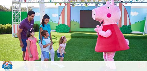 Family with kids meets a Peppa Pig mascot at a themed park.