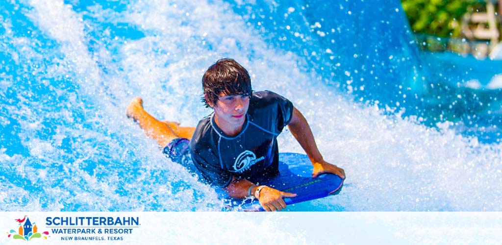 Image shows a person in a black and blue wetsuit bodyboarding on a vibrant blue artificial wave at Schlitterbahn Waterpark and Resort. The excitement of water sports is captured as the rider maintains balance amidst the dynamic splash of water.