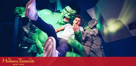 Image shows a person posing alongside a life-sized Hulk figure at Madame Tussauds New York. The vivid model of the Hulk captures a moment of action, and the individual is imitating being grabbed by the character, creating an engaging scene for visitors.