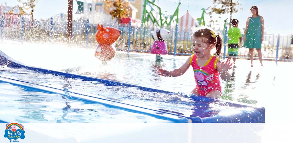 Child plays in water at a sunny park with people in the background.