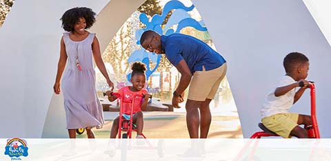 A family enjoys a sunny day at a playground with modern structures.