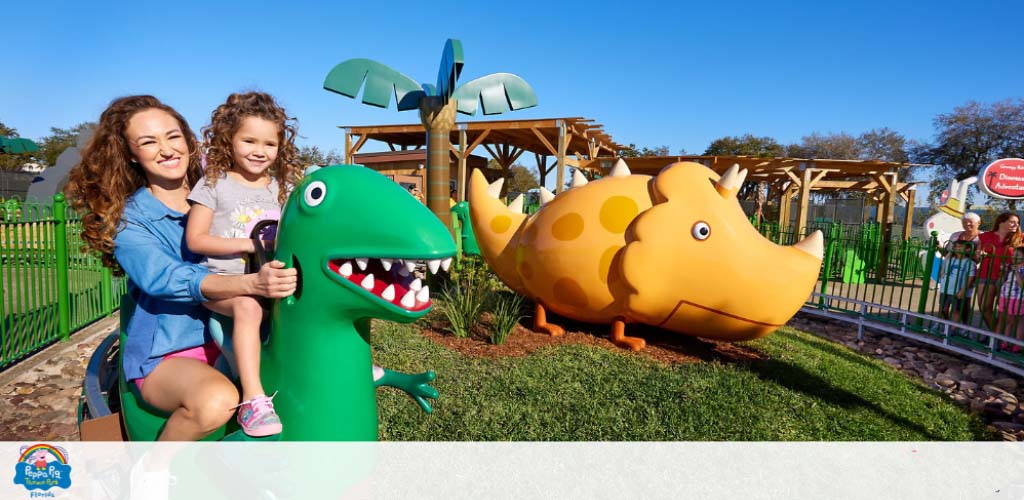 A woman and child enjoy a dinosaur ride at a sunny theme park.