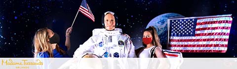 Astronaut figure with visitors holding a flag at Madame Tussauds against a space backdrop.