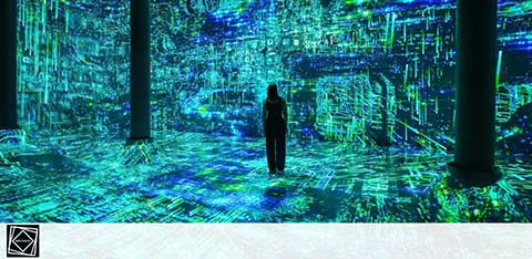 A person stands in a room with walls and floor immersed in a vibrant blue and green digital projection, resembling a circuit board. The space feels futuristic due to the seamless blend of light and patterns.