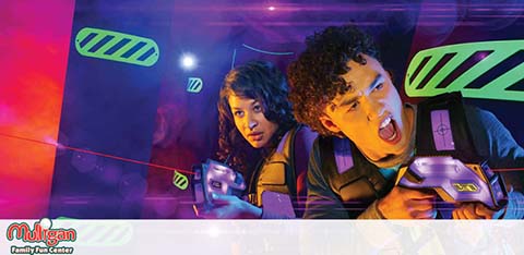 This image depicts an action-packed scene from a laser tag arena where two individuals appear engaged in the game. The arena is dimly lit with ambient purple and blue lighting adding to the futuristic atmosphere. Both participants are equipped with laser tag vests and are holding phasers, ready for play. The laser beams cut through the smoky air of the arena, as the players peek around a corner, with focused and excited expressions on their faces. The graphics and neon lights give the scenery a video game-like vibe, enhancing the overall excitement of the experience. In the foreground, the logo "Mulligan Family Fun Center" suggests the setting or the provider of this entertainment activity.

At GreatWorkPerks.com, we're committed to ensuring you enjoy such thrilling adventures at the lowest prices—earn unbeatable savings when you purchase your tickets with us!